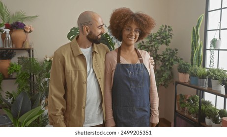 A man and a woman, possibly florists or gardeners, stand together amid colorful plants in the well-lit interior of a flower shop. - Powered by Shutterstock