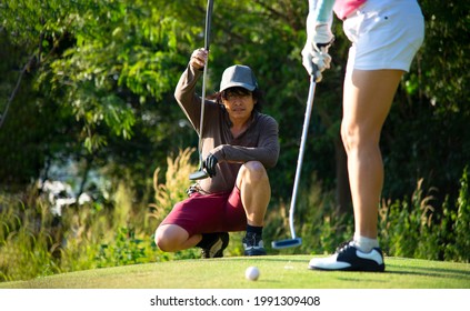 Man And Woman Practices Her Golf Swing On Driving Range
