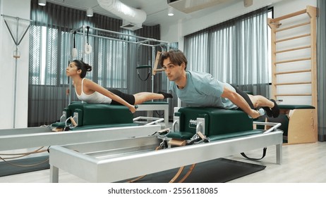 Man and woman practicing back extension exercises on pilates chair to strengthen core and back muscles at gym. Pilates partner prone extension on reformer for strengthening upper back. Habituate. - Powered by Shutterstock