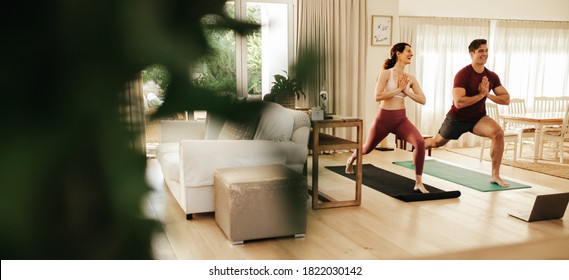 Man and woman practicing yoga at home with laptop in front. Couple watching fitness video tutorial online on laptop and doing yoga. - Powered by Shutterstock