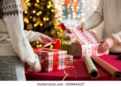 Man and woman preparing for Christmas. Couple in warm sweaters wrapping gifts. Decorated Christmas tree, boxes with presents, colourful wrapping paper and ribbons. 