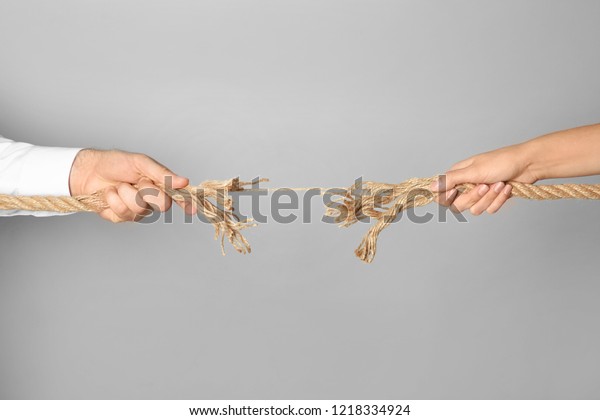 Man and woman pulling frayed rope at breaking\
point on gray background