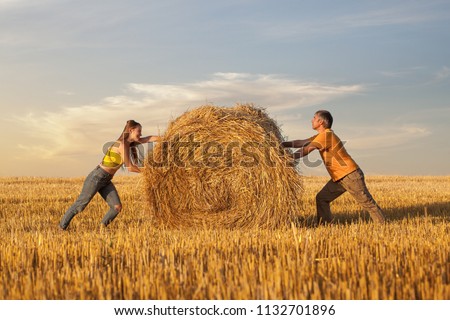 Man and woman pushing towards each other a straw bale. Concept of the dialectical principle of The Unity and The Struggle of Opposites
