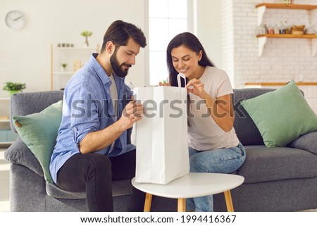 Man and woman relaxing at home on the weekend. Couple looks eagerly inside the package containing the food and drinks they ordered from the fast food service. Food delivery concept.