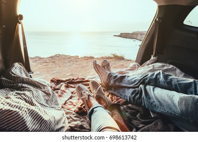 Man and woman relaxing inside trunk and watching at the sea. Fall car trip in sunset. Freedom travel concept. Autumn weekend.