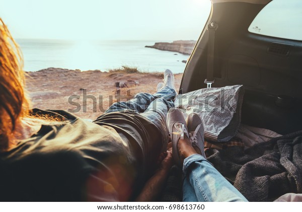Man and woman relaxing inside trunk and watching\
at the sea. Fall car trip in sunset. Freedom travel concept. Autumn\
weekend.