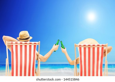 Man and woman relaxing on a beach and cheering with beer bottles