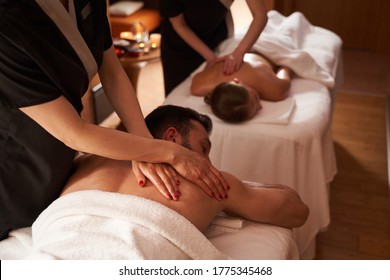 Man and woman relaxing on the couches. Hands of professional massage therapists gently touching their backs