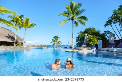 Man and Woman relaxing in a swimming pool, a couple on a honeymoon vacation in Mauritius tanning in the pool with palm trees and sun beds - Powered by Shutterstock