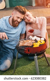 man and woman roasting meat and vegetables on barbecue grill, woman holding wineglass