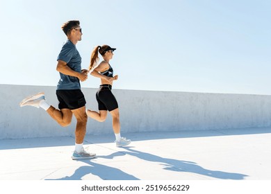 A man and woman run together on a rooftop, enjoying the sunny weather while engaging in their fitness routine. - Powered by Shutterstock