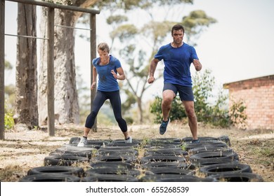 Man And Woman Running Over The Tyre During Obstacle Course In Boot Camp