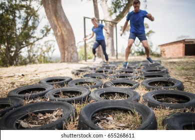 Man and woman running over the tyre during obstacle course in boot camp - Powered by Shutterstock