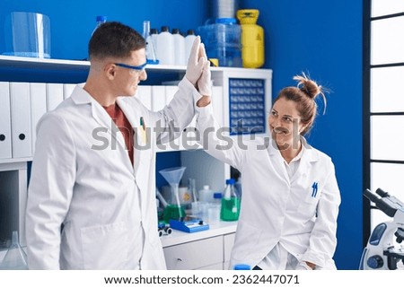 Man and woman scientists high five with hands raised up at laboratory