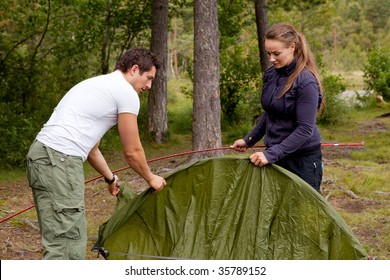 A Man And Woman Setting Up A Tent In The Forest