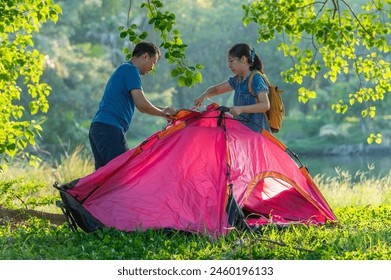 A man and a woman setting up a tent together in the woods - Powered by Shutterstock