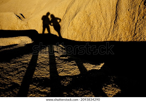 Man and woman shadow silhouettes projected\
over a dried mud ravine yellowed by the setting sun at Berca Mud\
Volcanoes reservation