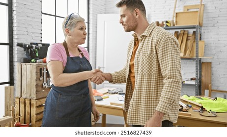 A man and woman shake hands in a woodworking workshop, surrounded by tools and lumber. - Powered by Shutterstock