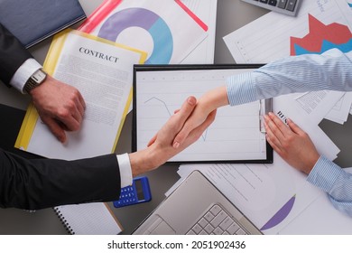 Man And Woman Shaking Hands Over Table With Financial Graphics.