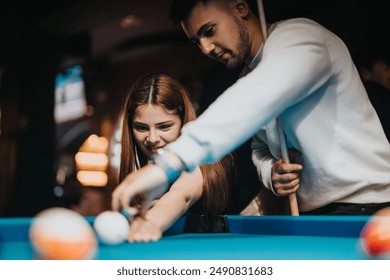 A man and woman share a playful moment while playing pool, surrounded by the warm ambiance of a billiard hall. - Powered by Shutterstock