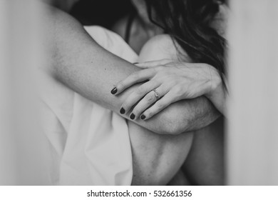 Man and woman in the sheets  sitting in front of the sill of the window.  Hands close-up.