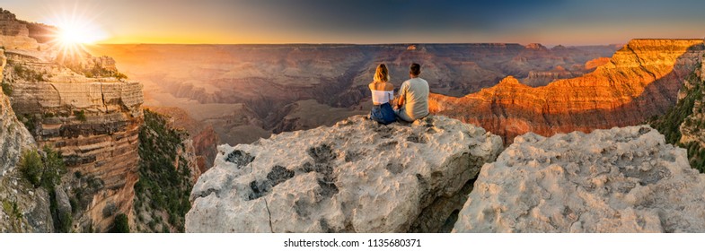 A man and a woman sit at the edge of the Grand Canyon at sunset minutes