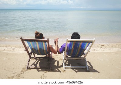 Man and Woman sit on beach chair, couple of hands against the sea view