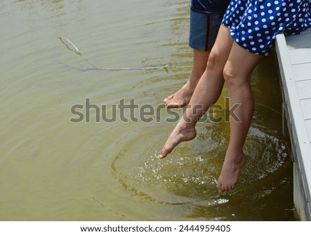 A man and a woman sit on a bridge and dangle their feet into a muddy creek in the countryside. 