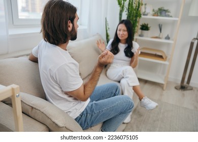 A man and a woman sit on the couch at home in white T-shirts and shouting communicate scandalously do not understand each other. A quarrel in the family of two spouses and aggression, sad emotions - Shutterstock ID 2236075105