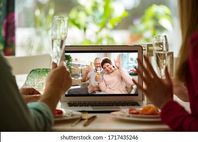 Man and woman sitting at the dining table, having dinner, drinking Champagne and having video call with senior parents on laptop. Staying home, quarantine and social distancing celebration of event.  - Powered by Shutterstock