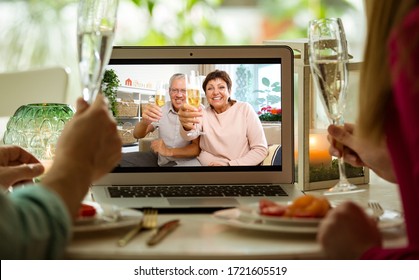 Mann und Frau sitzen am Esstisch, essen, trinken Champagner trinken und haben Videoanrufe mit Senioren auf dem Laptop. Die Feier des Ereignisses, zu Hause, unter Quarantäne und in sozialer Distanz zu bleiben. 