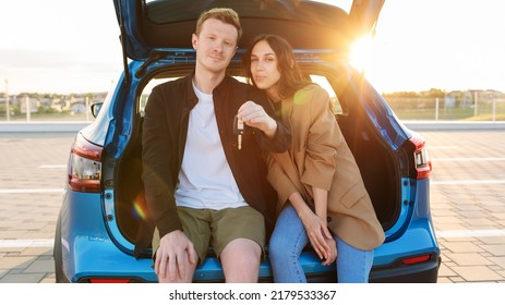 A man and a woman are sitting in a new car. Buying a car from a dealership. Models pose against the sunset