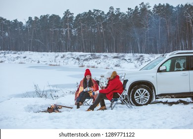 Man With Woman Sitting On Chairs Near Camp Fire In Winter Time. Car Travel. Active Lifestyle