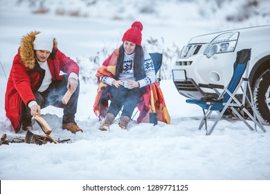 Man With Woman Sitting On Chairs Near Camp Fire In Winter Time. Car Travel. Active Lifestyle