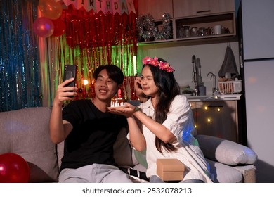 A man and woman are sitting on a couch, taking a selfie together. The woman is wearing a flower headband - Powered by Shutterstock