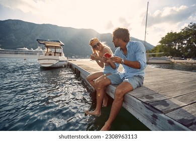 Man and woman sitting on the lake pier dangling legs and eat watermelon  together - Powered by Shutterstock