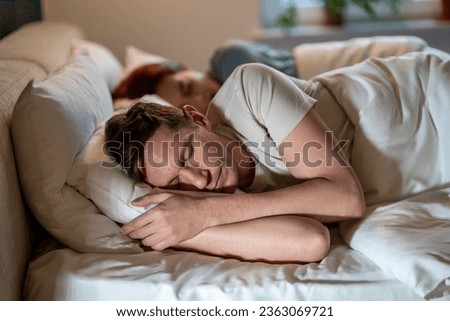 Man and woman sleep soundly well. Guy and girl dozing on same bed on soft regular comfortable pillows under warm blankets in glow of lights. Importance of long, healthy sleep. Joint sleep of spouses