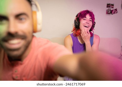 A man and a woman are smiling at the camera while wearing headphones. The woman is wearing a purple tank top and the man is wearing a red shirt - Powered by Shutterstock