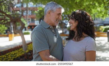 Man and woman smiling lovingly at each other in a sunny urban park, surrounded by greenery, showcasing a middle-aged couple in a joyful, romantic relationship outdoors. - Powered by Shutterstock