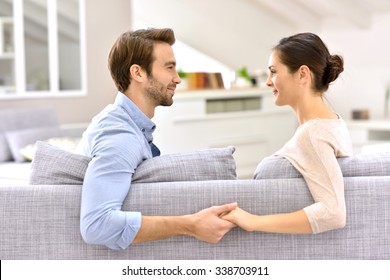 Man and woman in sofa, facing each other and holding hands