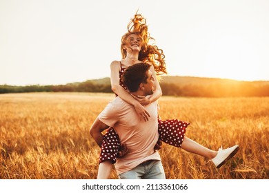 Man and woman spending Valentine's Day walking in the wheat field, smiling and having fun together. Man giving his girlfriend piggy-back wheat field. Healthy