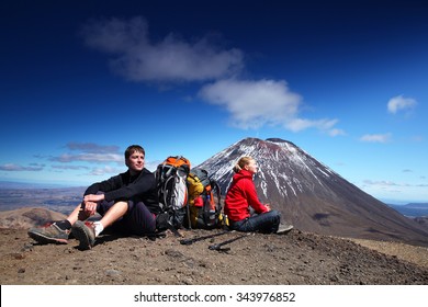 man and woman in sport clothing sitting in front of Tongariro volcano - Tongariro alpine crossing,  New Zealand