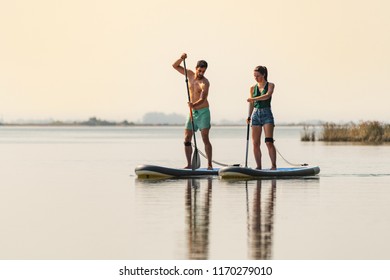 Man and woman stand up paddleboarding on lake. Young couple are doing watersport on lake. Male and female tourists during summer vacation. - Powered by Shutterstock