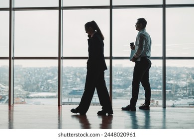 A man and a woman are standing in the office against the background of a large panoramic window. Modern spacious workspace with employees. Business partners - Powered by Shutterstock