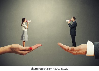 man and woman standing on the big palms and screaming at each other over dark background