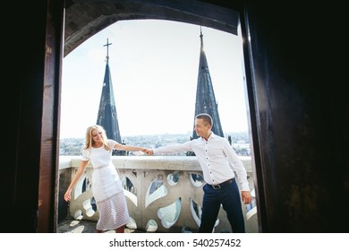 Man and woman stretch their hands while they stand on old balcony with great cityscape behind - Powered by Shutterstock