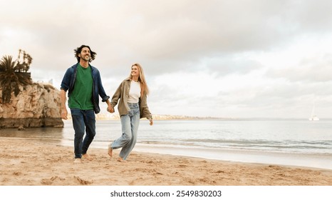 A man and woman stroll barefoot on the sandy beach, holding hands as they enjoy each other's company. The sun sets behind the clouds, casting a warm glow on the peaceful shoreline, copy space - Powered by Shutterstock