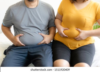 Man and woman suffering from extra weight. Paunch of the woman and man sitting on the bed