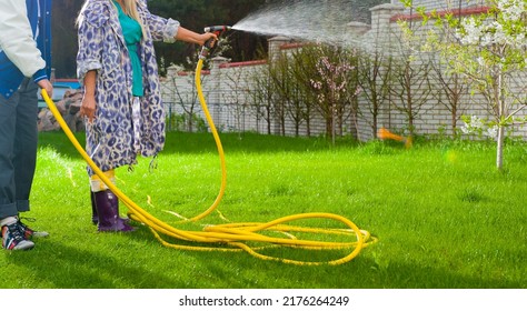 A Man And A Woman Take Care Of The Lawn Grass. A Family Couple Mows The Grass Watering The Grass