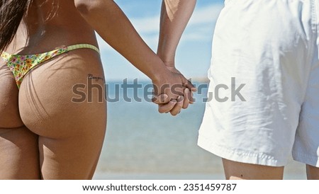 Man and woman tourist couple standing with hands together backwards at beach